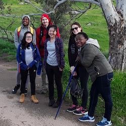 Six graduate students posted in front of tree while on hike