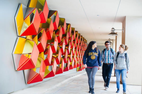 Three students walking next to geometric wall display