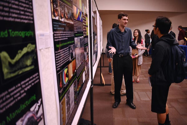 student explaining research poster to another student