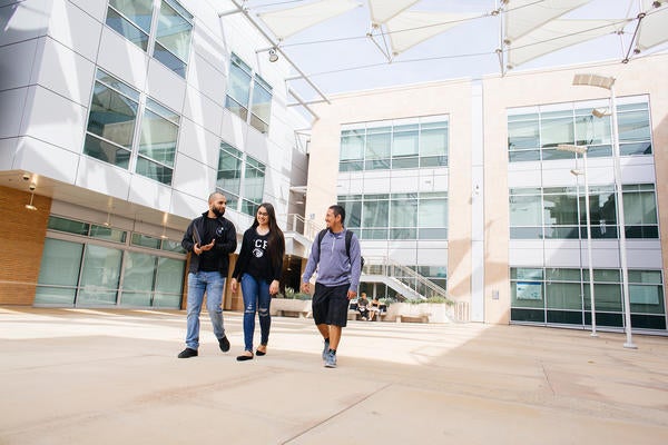 Three students walking in a courtyard between buildings